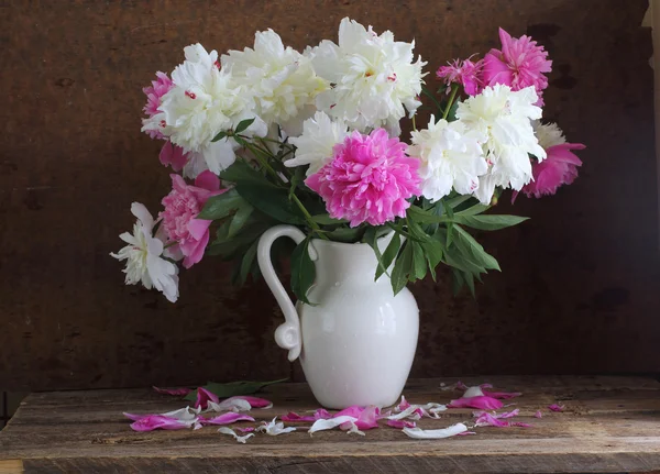 Bouquet from pink and white peonies in a white jug on a wooden t