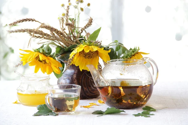 Tea in a transparent teapot, honey and sunflowers in a ceramic v