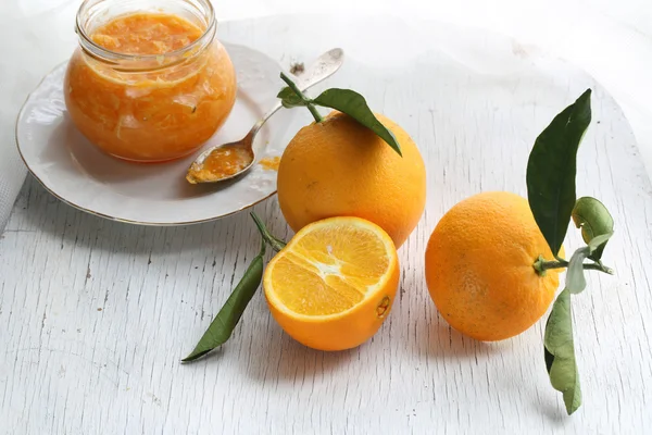 Orange confiture in a glass jar and fresh oranges