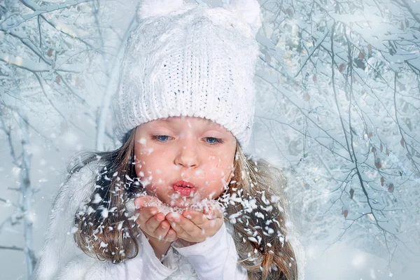 The beautiful little girl blows off snow from palms