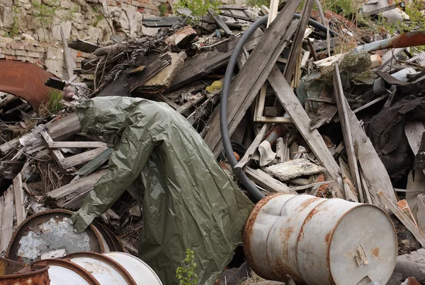 Man with gas mask and green military clothes explores barrels after chemical disaster.