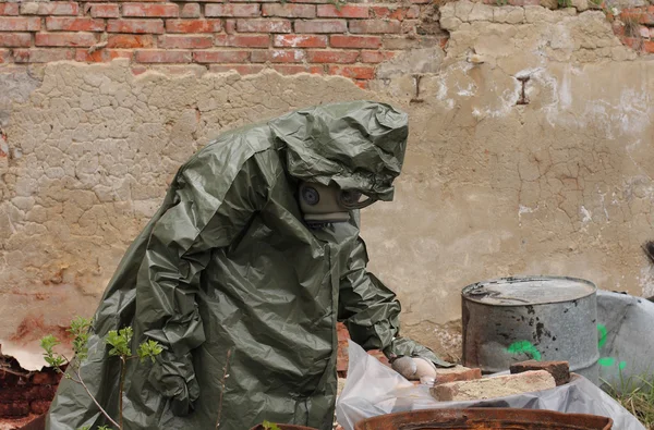 Man with gas mask and green military clothes explores dead bird after chemical disaster.