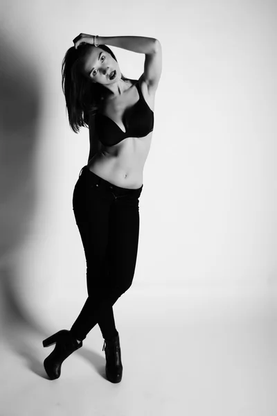 Black and white photo of beautiful brunette woman model  posing in studio. Wearing jeans, bra, heels