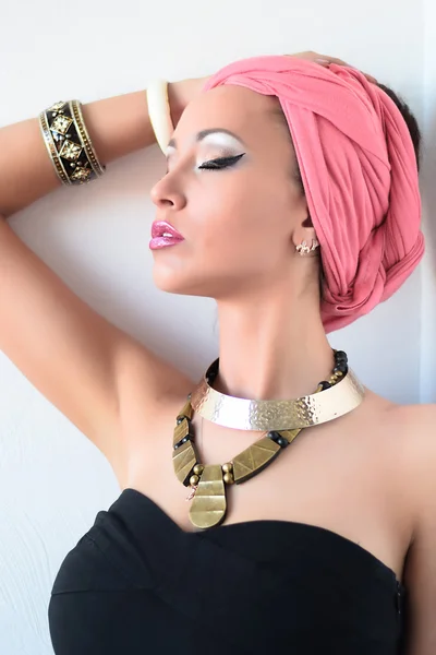 Portrait of beautiful white-skinned girl in pink turban and black dress, african queen style. White background