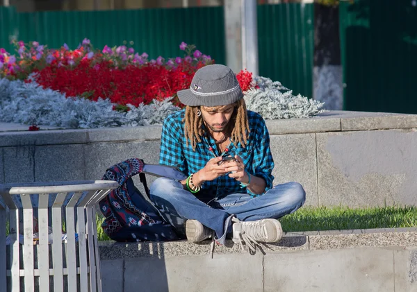 Kiev, Ukraine - September 09, 2015: Young man with dreadlocks listening to music while sitting on the curb