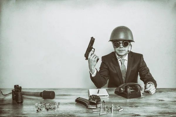 Vintage military businessman sitting at office desk with hand gun