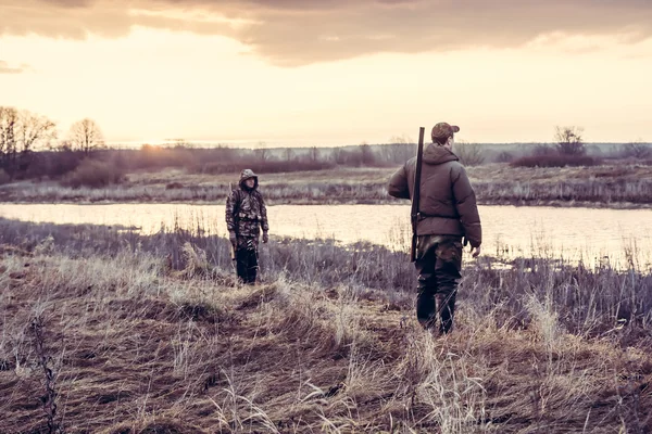Hunters choosing a good position  for duck hunting in field nearby river during sunrise