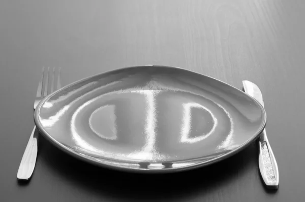 Black and white shot of an empty plate with fork and knife next to it