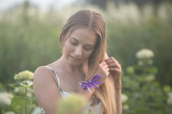 Young beautiful woman in the warm rays of the evening sun walking on a green field with white flowers.