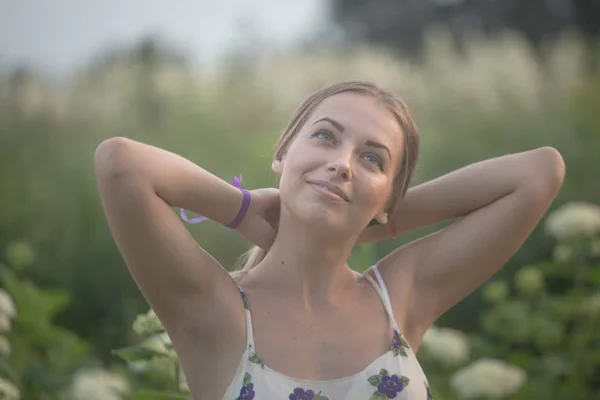 Young beautiful woman in the warm rays of the evening sun walking on a green field with white flowers.