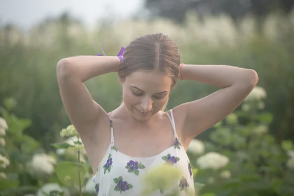 Young beautiful woman in the warm rays of the evening sun walking on a green field with white flowers.