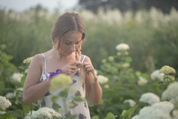 Young beautiful woman in the warm rays of the evening sun walking on a green field with white flowers.