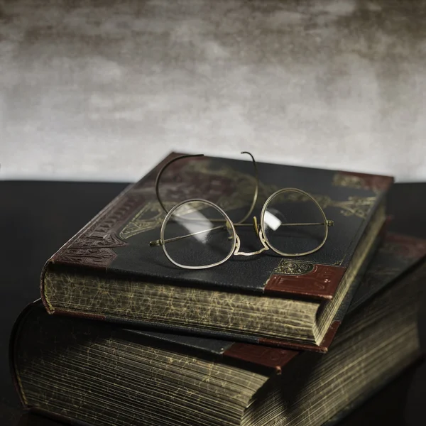 Two old books with antique reading glasses on grey