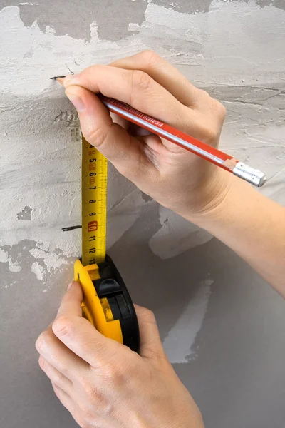 Hands measuring wall with tape measure