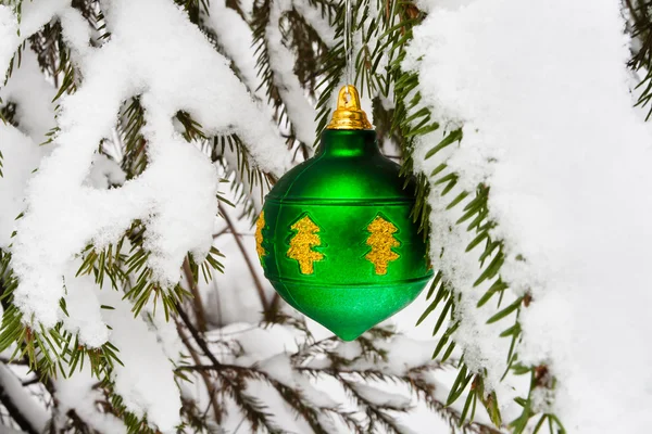 Green Christmas ball on snowy fir tree