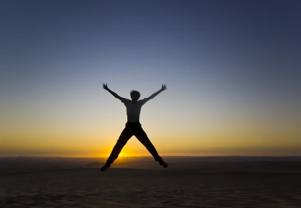 Jumping man with hands up at sunset in desert