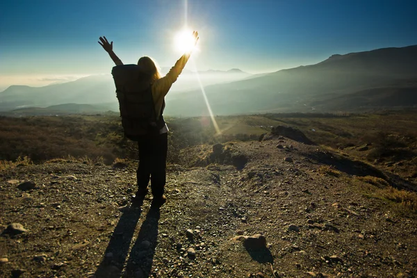 Girl-backpacker with hands up in the mountains against sun