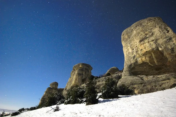 Moon lights big rock with snow on hills