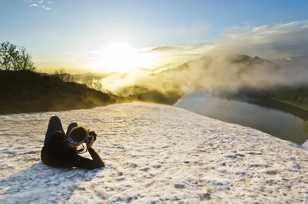 Man on a snow at sunset with camera making photo