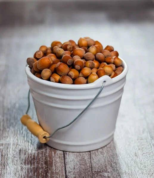 Hazelnuts in a white bucket on a wooden background