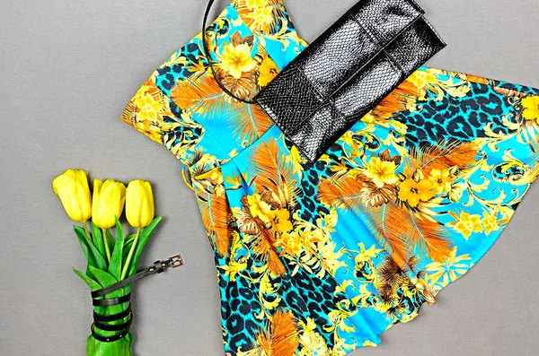Dress with floral print, yellow tulips and black clutch on gray
