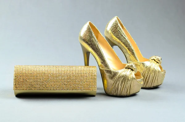 Gold high-heeled shoes and clutch bag on a gray background