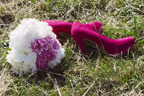 Wedding bouquet and bride\'s pink shoes lie on the grass in the park