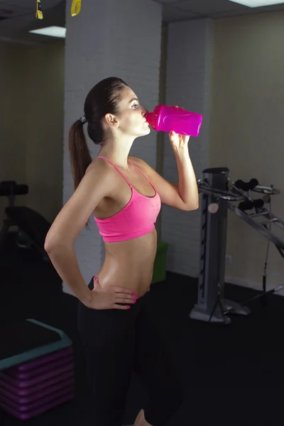 Beautiful girl fitness trainer drinking water from a bottle after a workout shaker