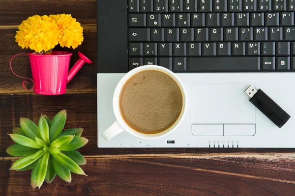 Notebook computer with coffee cup, computer and flower. View fro