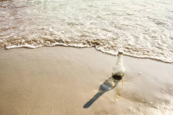 Empty glass bottle washed up as rubbish on a beach, garbage on b