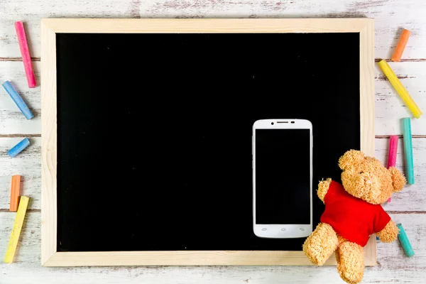 Blank blackboard, Teddy Bear and smart phone on wooden table.Tem
