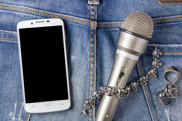 Smartphone, bracelet, Ring and microphone on jeans background.Ro