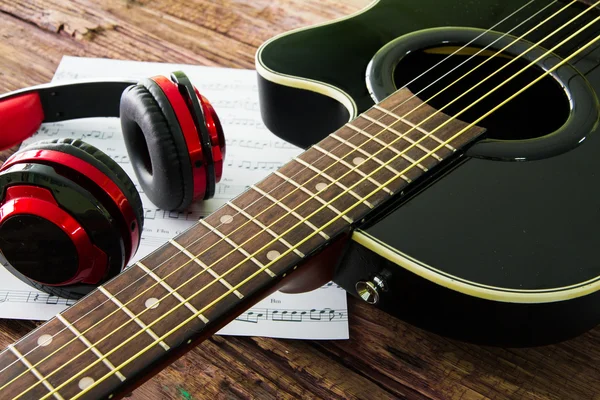 Acoustic guitar, headphones and sheet musical noteson the table