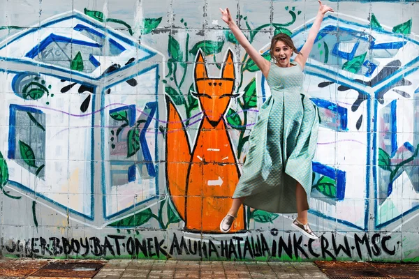 Young happy girl in a dress jumping, background graffiti