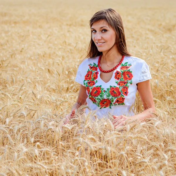 Beauty girl outdoors on the wheat field, woman dressed in national dress. Blowing long hair.