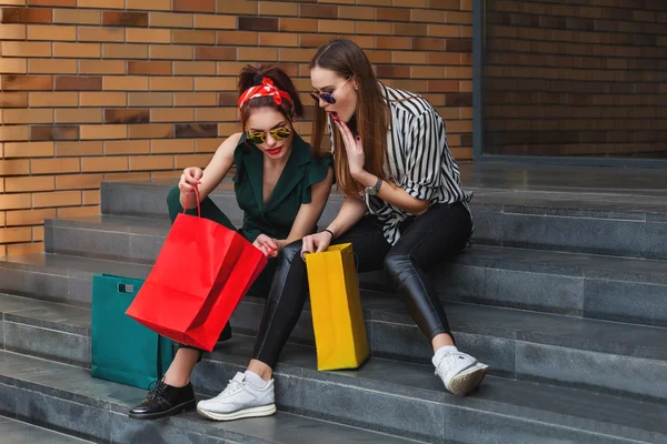 Beautiful fashion women sitting on stairway with shopping bags. Trendy lifestyle urban portrait.