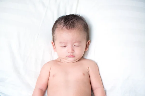 Cute Asian baby sleeping on a white pillow, on bed