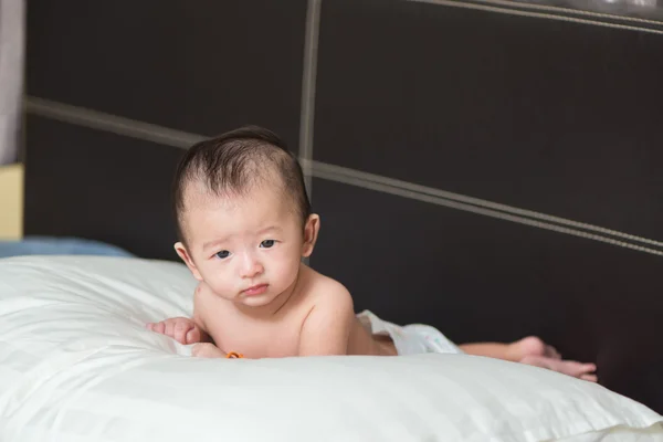 Unhappy Cute Asian baby lying on a white pillow, on bed