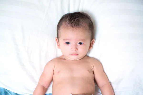 Cute Asian baby lying on a white pillow, on bed