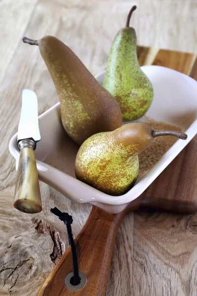 Three pears in baking dish, sugar and knife