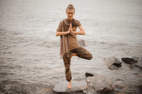 Woman doing yoga tree pose namaste on the stone near the ocean