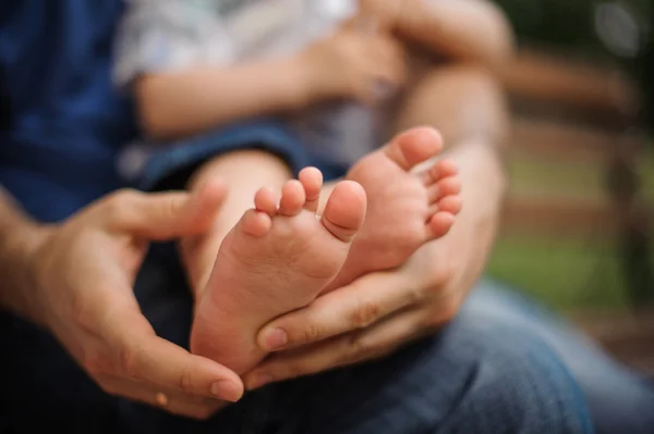 Little baby feet in daddys hands on nature outdoors. summer park in background.