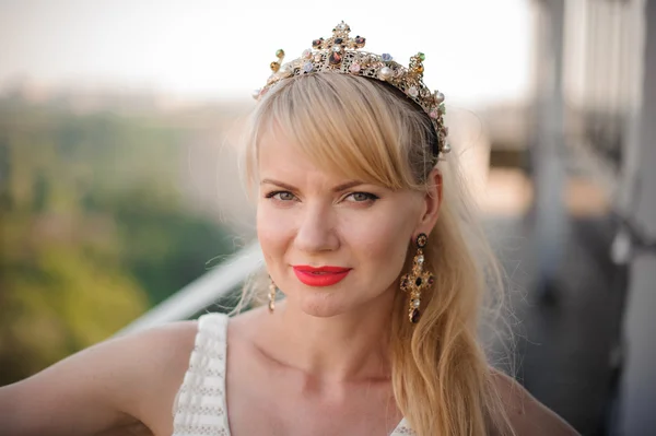 Beautiful blonde woman with long hair wearing crown decorated gemstones.
