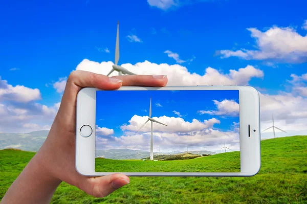 Hand holding smart phone take a photo at Wind turbines generating electricity.