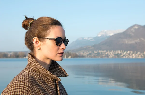 Beautiful woman in sunglasses on a background of lake and mountains.