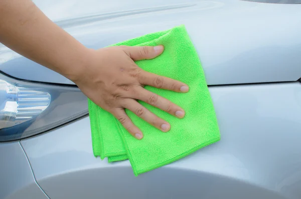 Hand with green microfiber cloth cleaning car.