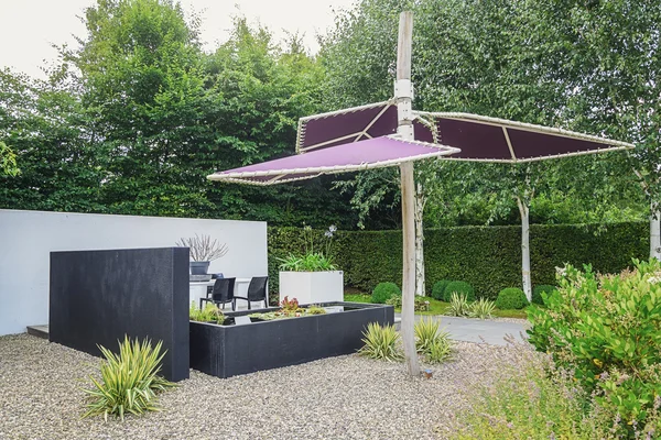 Garden with modern garden furniture,  trendy pond and parasol.