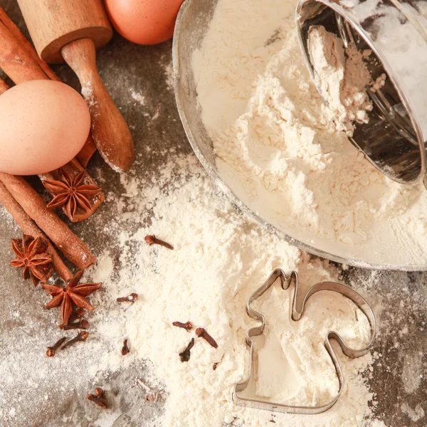 Flour in a metal bowl with  wooden rolling pin on  stone table.