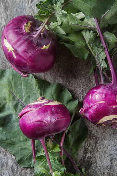 Ripe purple turnips with green leaves. Grey stone background. Au