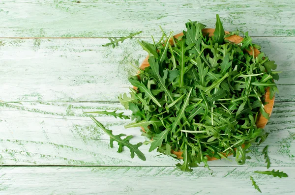 Fresh green arugula in bowl on wooden table